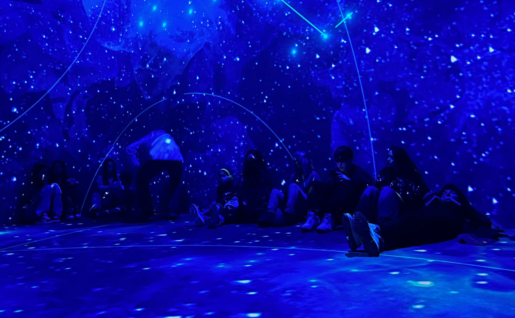 Fabrique des Lumières exhibition — visitors immersed in blue starfield projection covering floor, walls, and ceiling